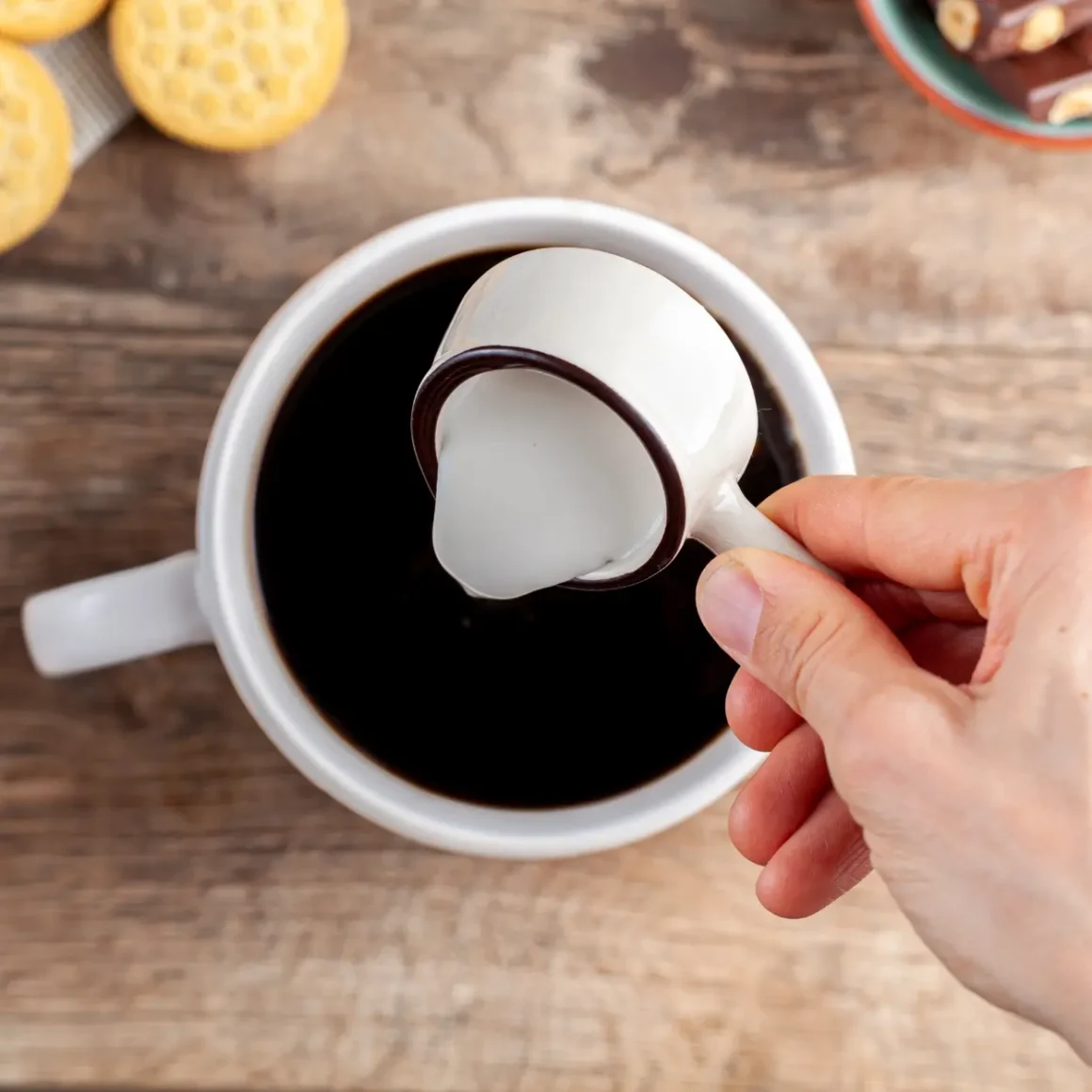 a person pouring a coffee creamer into a cup of coffee