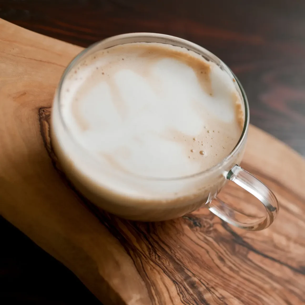 a glass cup of latte on a wood surface