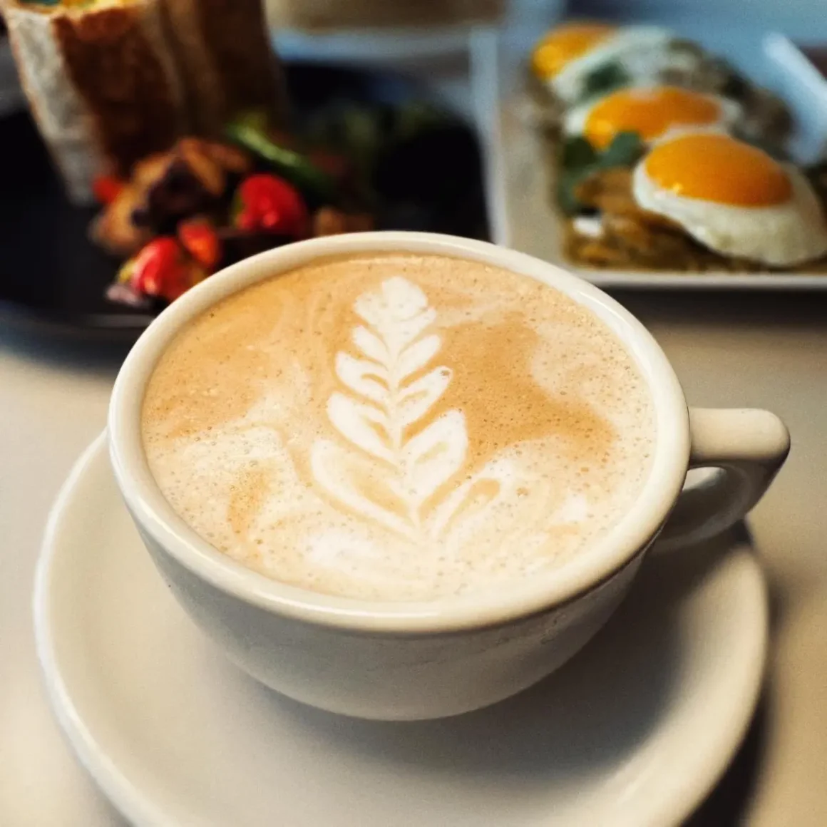 a cup of latte with a leaf design in the foam