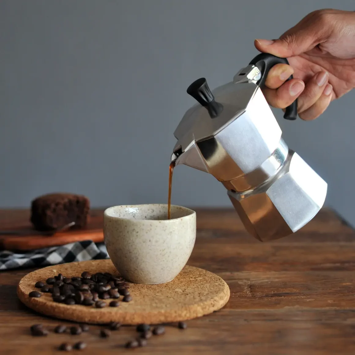 a hand pouring coffee from a moka pot into a cup