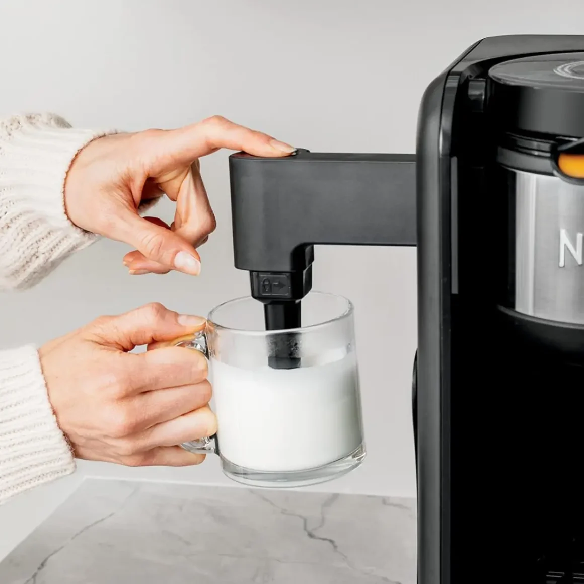 a hand holding a cup pouring from a coffee maker