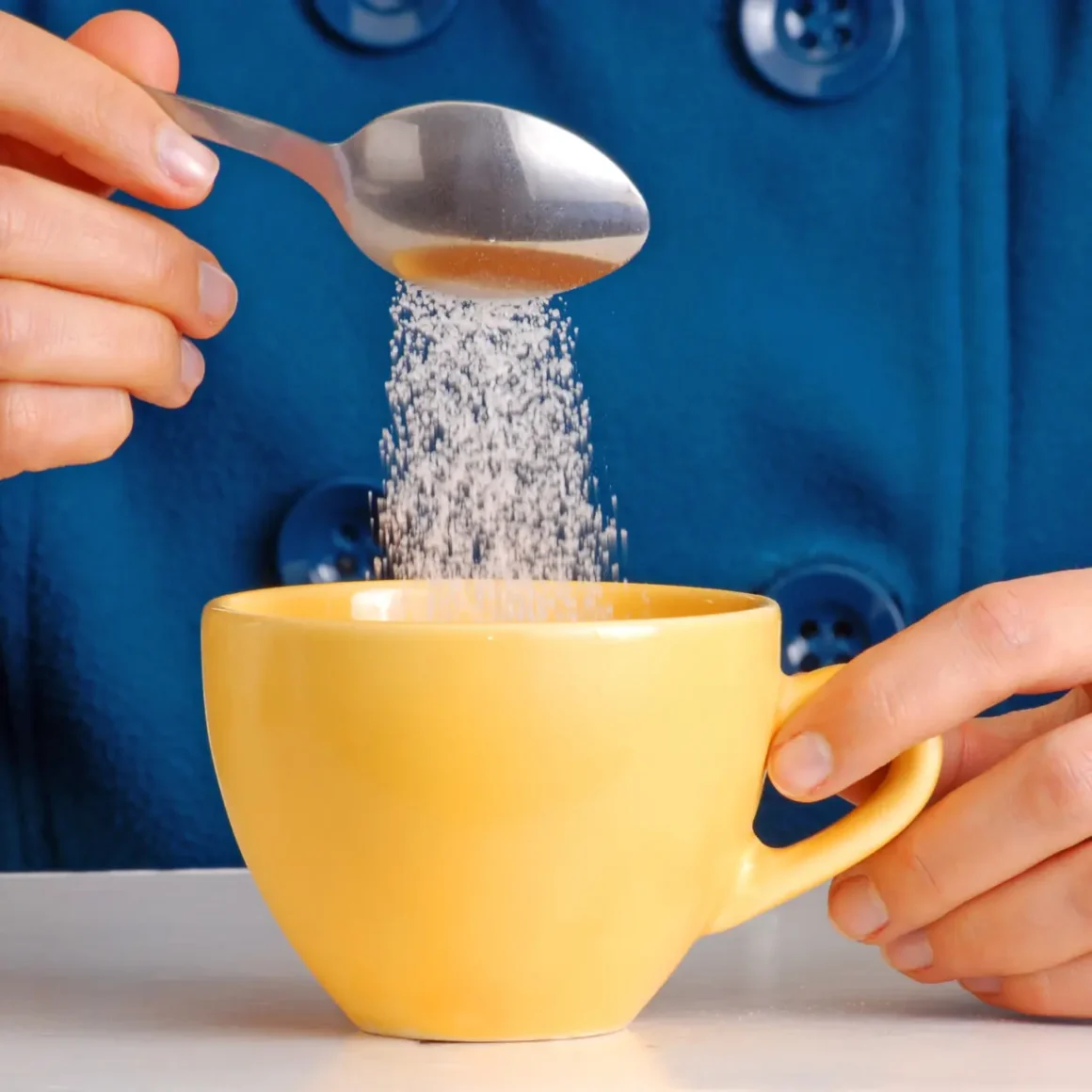 a person pouring sugar into a yellow cup
