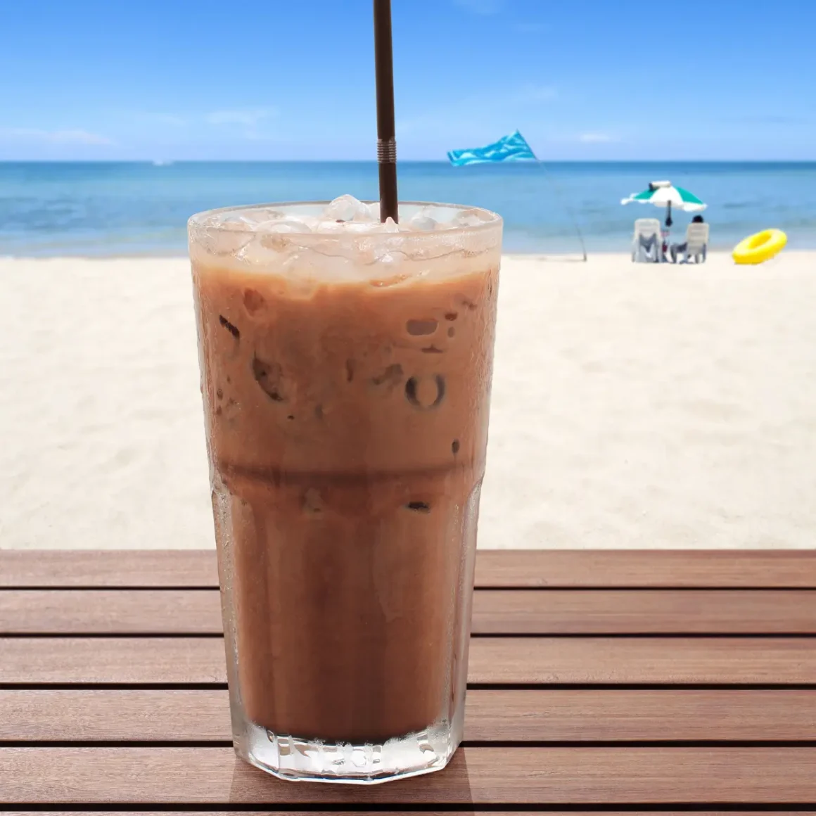a glass of cold latte with a straw on a table on a beach
