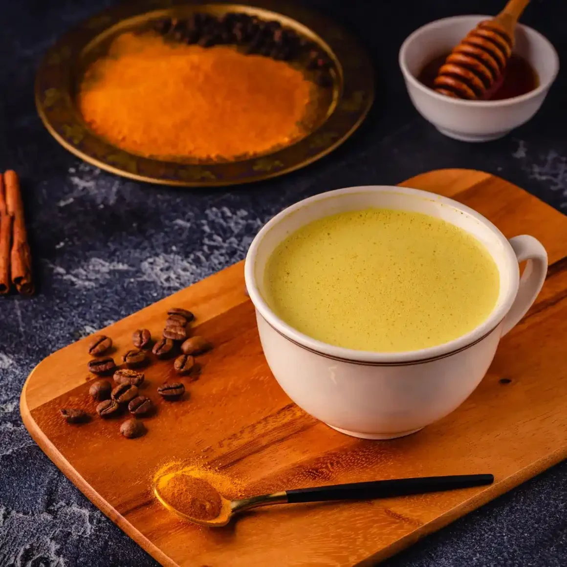 a cup of turmeric coffee with a spoon and coffee beans on a wooden board
