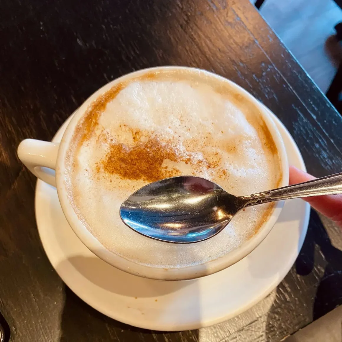 a hand holding a cup of cafe con leche with a spoon