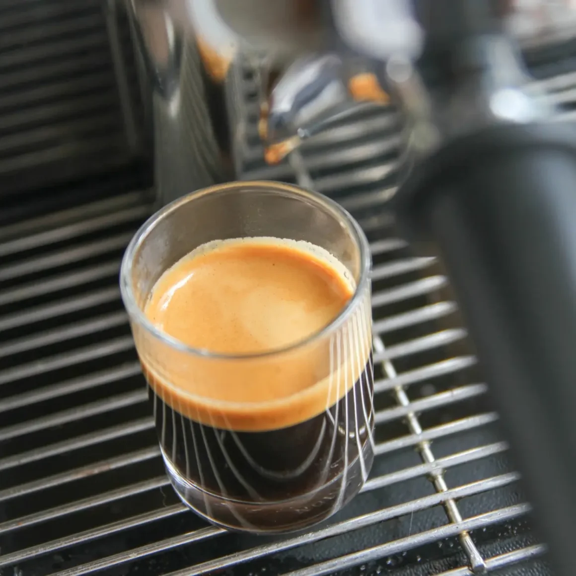 a glass of espresso on a metal grate