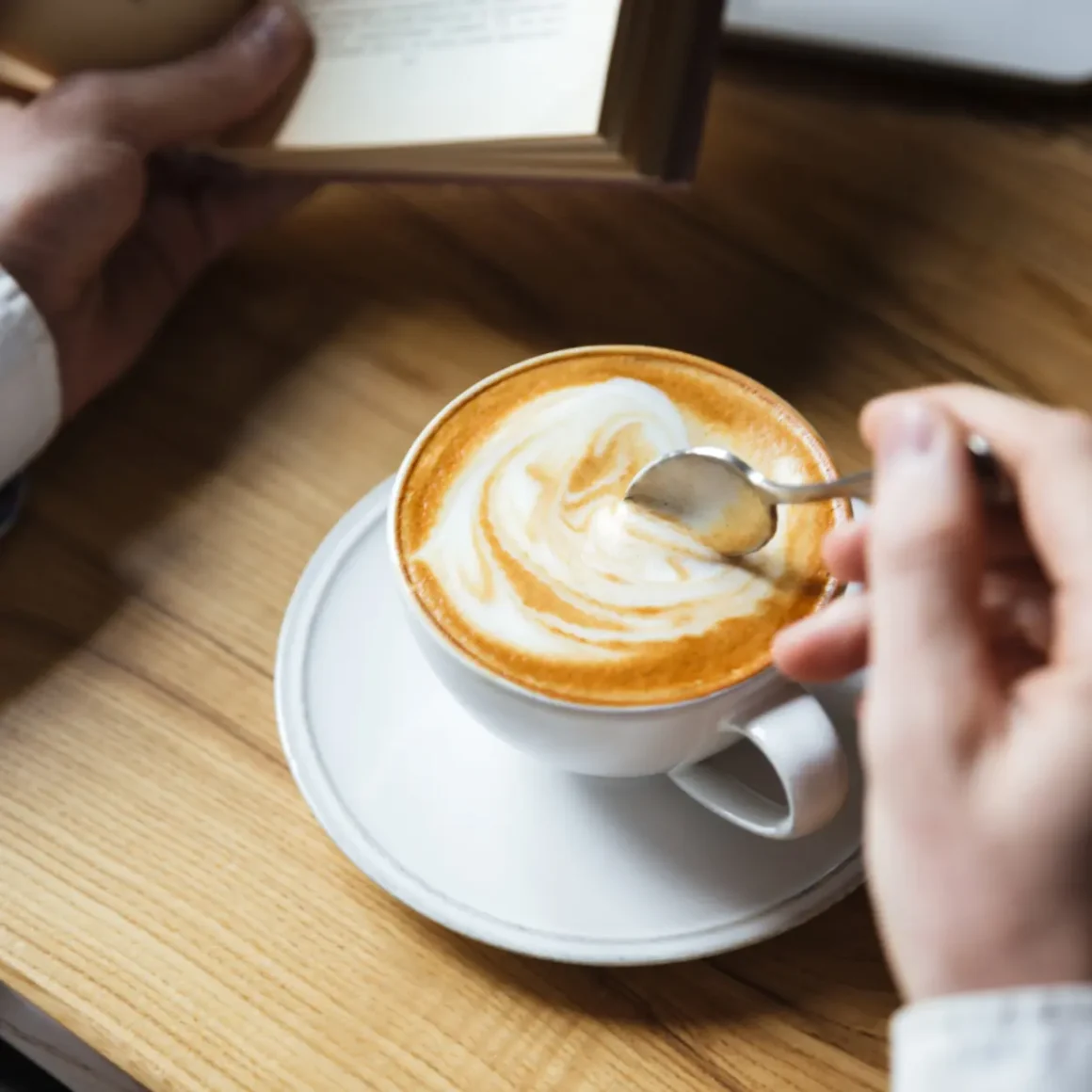 a hand holding a spoon over a cup of oat milk cappuccino