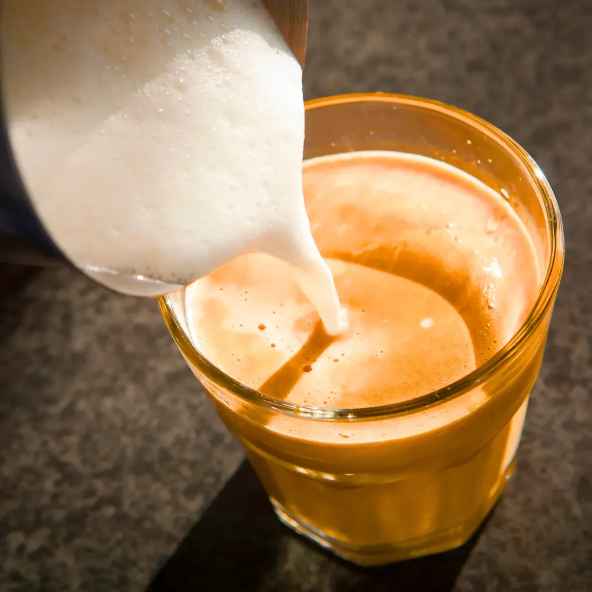 barista pouring coffee creamer into a glass of coffee