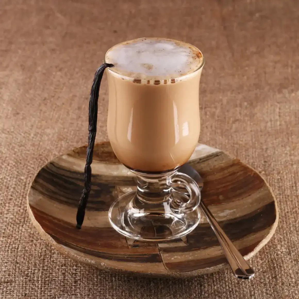 a glass of vanilla latte with a vanilla stick on a plate