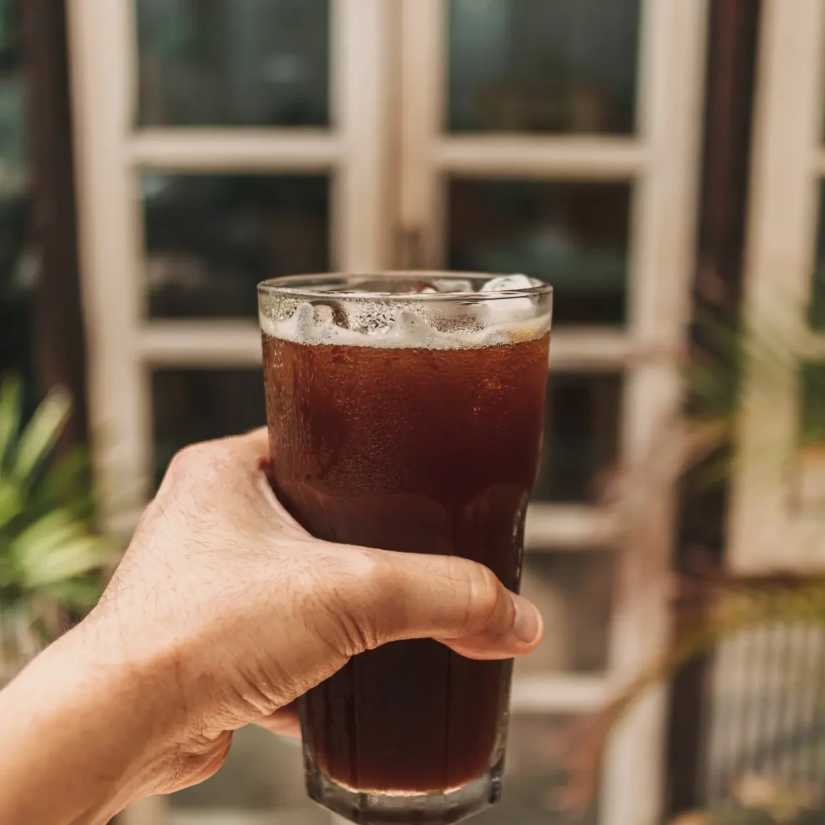 a hand holding a glass of cold brew coffee