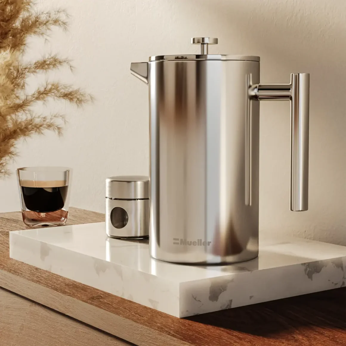 a silver mueller french press coffee maker and a glass of coffee on a marble counter